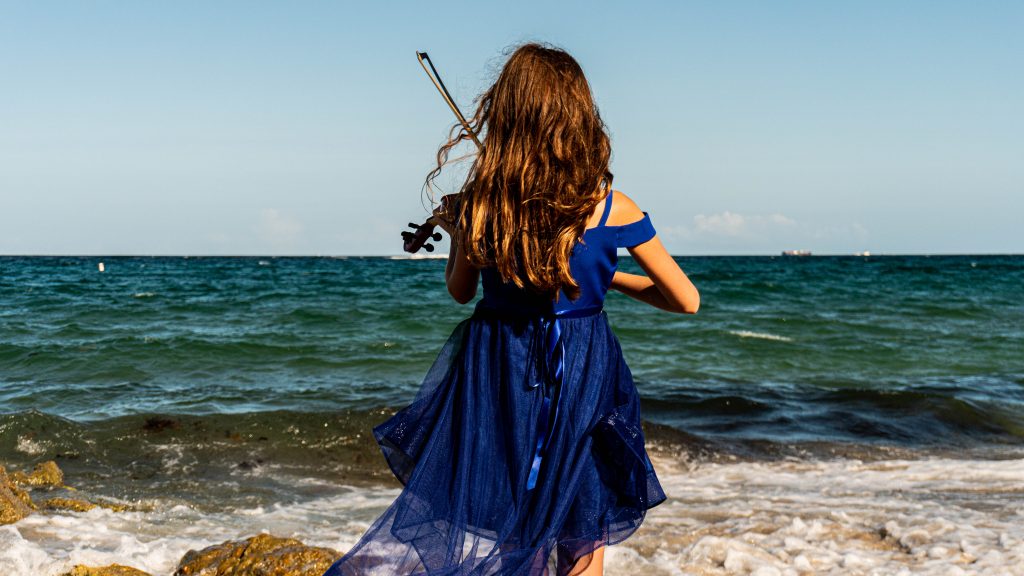 violin student facing the ocean's horizon.