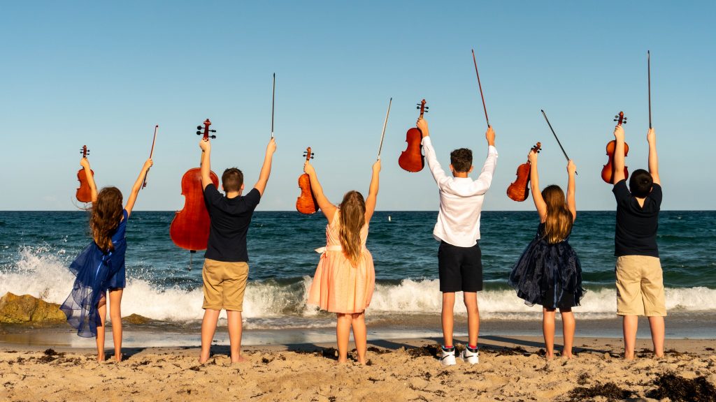 Group of students standing in the sand, holding their instruments in the air.